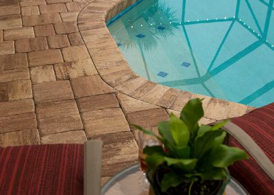 Paved poolside with red-striped chairs, potted plant, and blue water reflecting pool lights.