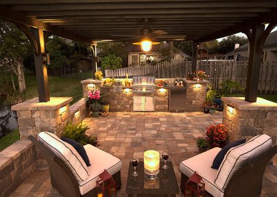 Covered patio with outdoor kitchen, grill, two chairs, table with candle, and wine glasses at sunset.